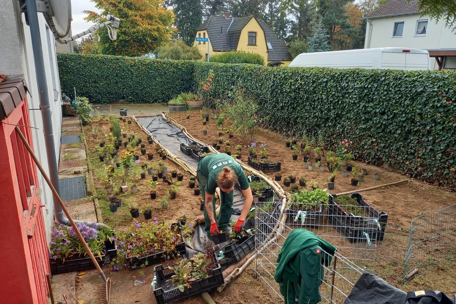 Mitarbeiter bewässert eine neu angelegte Pflanzfläche mit Stauden, Natursteinen und offenem Boden in einem naturnahen Garten.